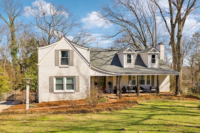 view of front facade featuring a porch, a front yard, brick siding, and a chimney