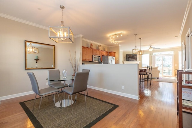 dining area with light wood-type flooring, baseboards, crown molding, and ceiling fan with notable chandelier