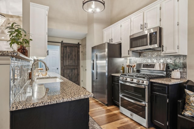 kitchen with appliances with stainless steel finishes, light stone counters, white cabinets, a barn door, and sink