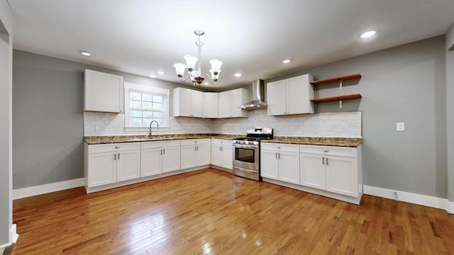 kitchen with wall chimney exhaust hood, sink, stainless steel gas range oven, white cabinetry, and pendant lighting