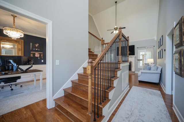 stairs with hardwood / wood-style flooring, ornamental molding, ceiling fan with notable chandelier, and high vaulted ceiling