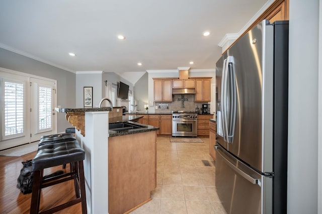 kitchen featuring light tile patterned floors, backsplash, stainless steel appliances, a kitchen bar, and dark stone counters