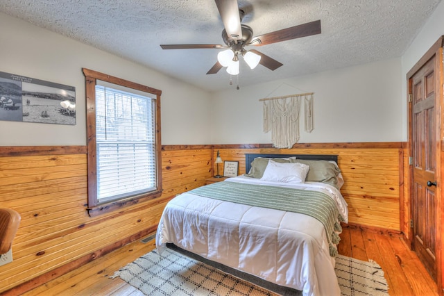 bedroom featuring hardwood / wood-style floors, a textured ceiling, and wooden walls