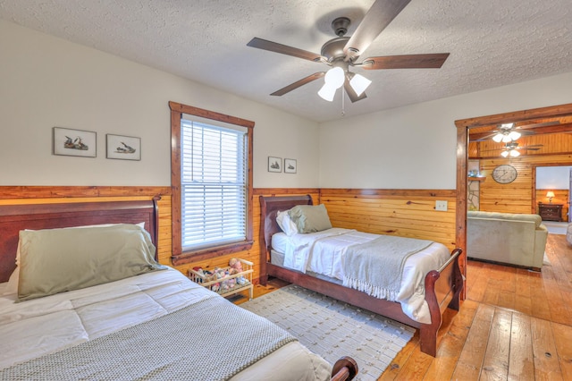 bedroom with ceiling fan, light hardwood / wood-style floors, a textured ceiling, and wood walls