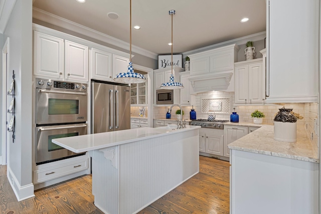 kitchen featuring hardwood / wood-style flooring, stainless steel appliances, an island with sink, white cabinets, and decorative light fixtures