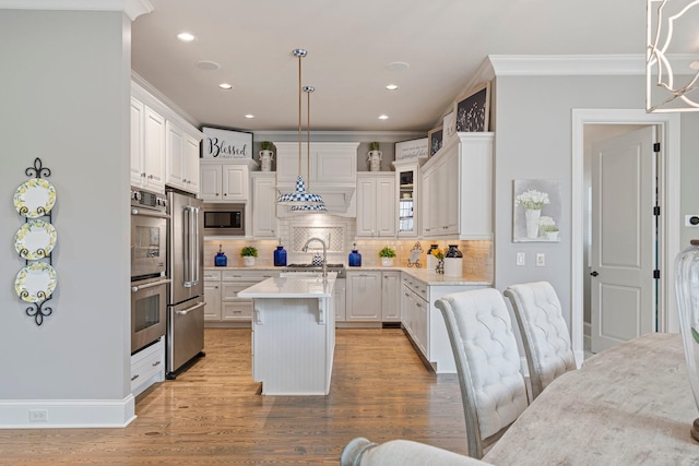 kitchen featuring hanging light fixtures, a center island with sink, ornamental molding, appliances with stainless steel finishes, and white cabinets