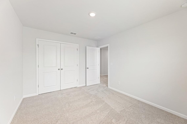 unfurnished bedroom with light colored carpet and a closet