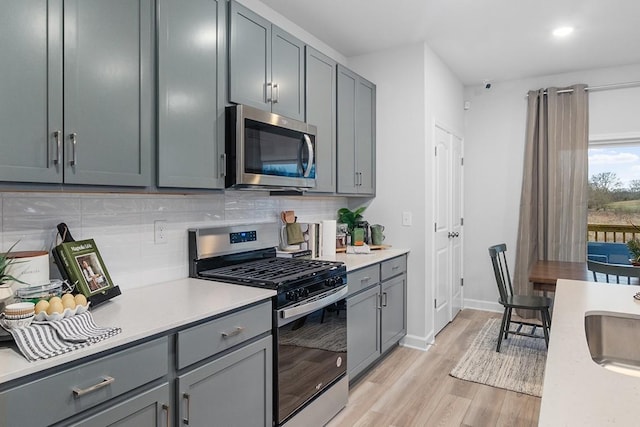 kitchen with gray cabinetry, tasteful backsplash, stainless steel appliances, and light wood-type flooring