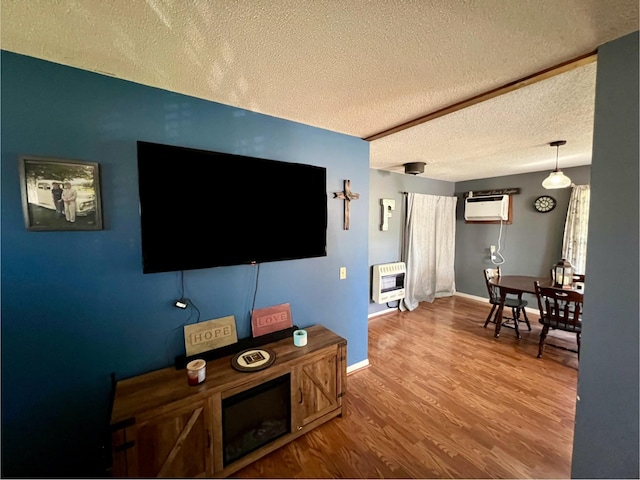 living room featuring wood-type flooring, a wall mounted air conditioner, heating unit, and a textured ceiling