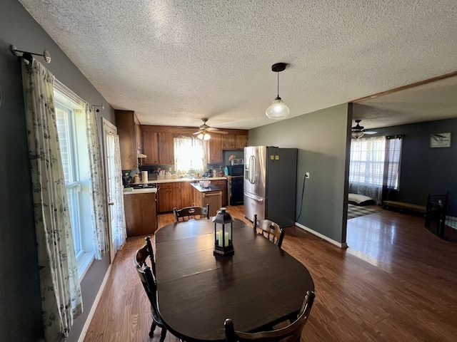 dining room with ceiling fan, a textured ceiling, dark hardwood / wood-style floors, and a healthy amount of sunlight