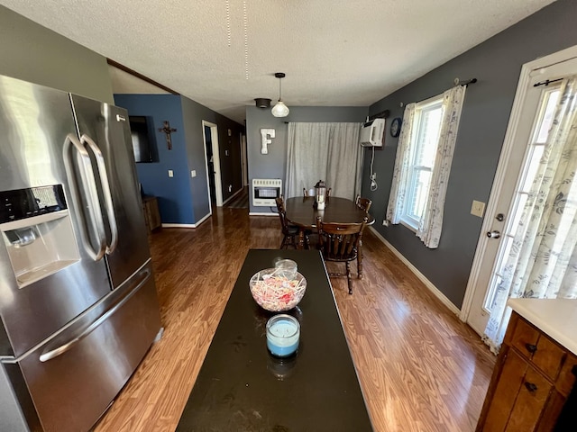 dining area with a wall mounted air conditioner, hardwood / wood-style floors, heating unit, and a textured ceiling