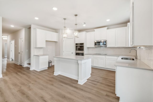 kitchen featuring a kitchen island, a sink, white cabinetry, appliances with stainless steel finishes, and backsplash