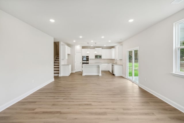 unfurnished living room with stairway, light wood-style flooring, baseboards, and recessed lighting