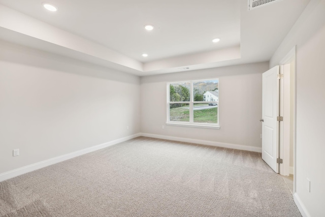 spare room featuring light carpet, recessed lighting, a raised ceiling, and baseboards