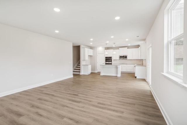 unfurnished living room featuring light wood finished floors, baseboards, stairs, a sink, and recessed lighting