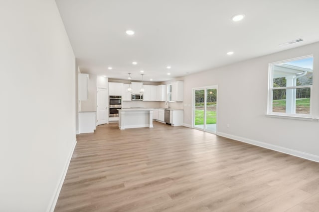 unfurnished living room featuring light wood-type flooring, visible vents, and baseboards