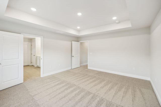 empty room featuring baseboards, a tray ceiling, and light colored carpet