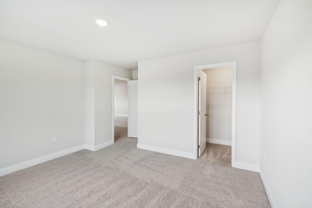 unfurnished bedroom with carpet floors, a walk in closet, baseboards, and recessed lighting