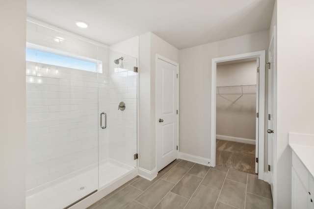 full bathroom with a spacious closet, a shower stall, vanity, and baseboards