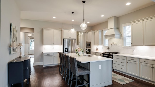 kitchen featuring sink, hanging light fixtures, a center island with sink, appliances with stainless steel finishes, and custom range hood