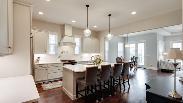 kitchen with hanging light fixtures, sink, a kitchen island with sink, and custom range hood