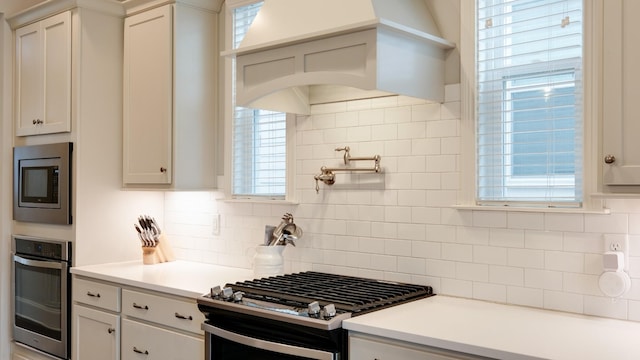 kitchen with a healthy amount of sunlight, decorative backsplash, stainless steel appliances, and white cabinets