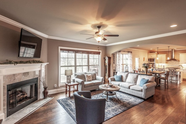 living room with a fireplace, crown molding, dark wood-type flooring, and ceiling fan