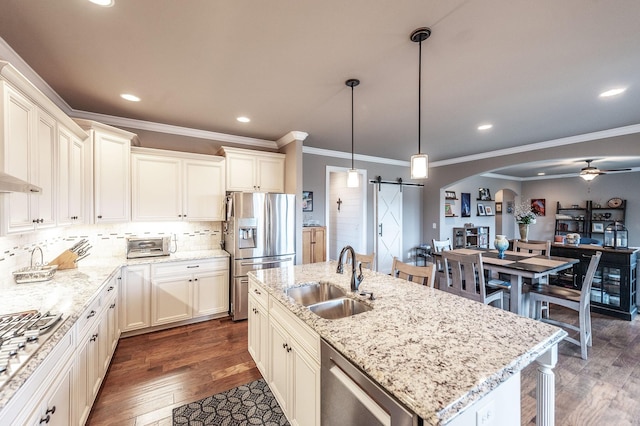 kitchen with appliances with stainless steel finishes, sink, hanging light fixtures, a barn door, and a center island with sink