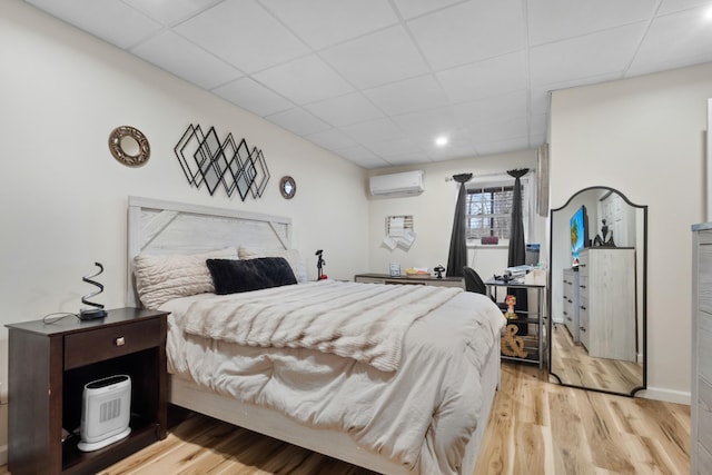 bedroom featuring a wall mounted AC, light hardwood / wood-style floors, and a drop ceiling