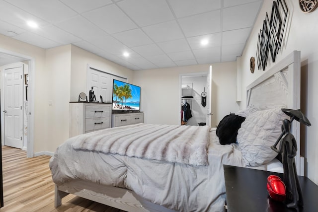 bedroom with a closet, a spacious closet, a drop ceiling, and light hardwood / wood-style flooring