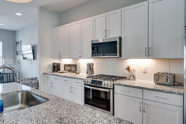 kitchen with tasteful backsplash, sink, white cabinets, and appliances with stainless steel finishes