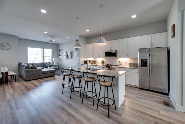 kitchen with a breakfast bar, dark stone counters, an island with sink, stainless steel appliances, and white cabinets