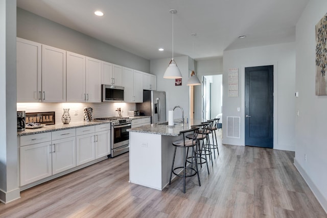 kitchen featuring white cabinetry, hanging light fixtures, light stone countertops, and appliances with stainless steel finishes