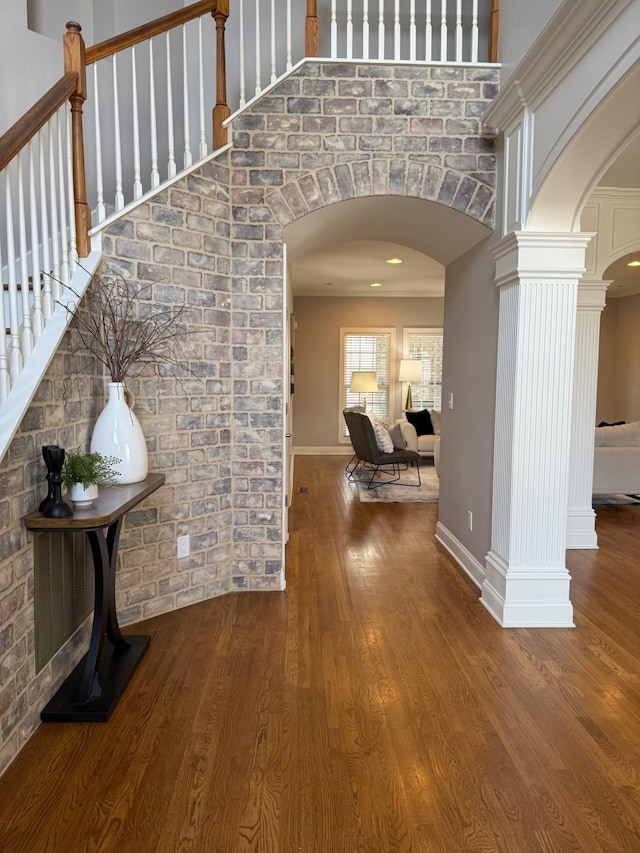 hallway with baseboards, decorative columns, a towering ceiling, wood finished floors, and arched walkways