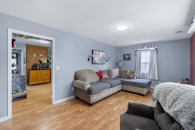 living room featuring a textured ceiling, light wood-type flooring, visible vents, and baseboards