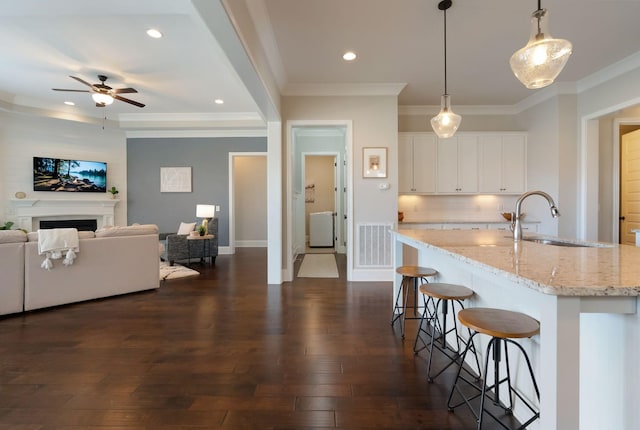 kitchen with white cabinetry, sink, hanging light fixtures, light stone counters, and a center island with sink