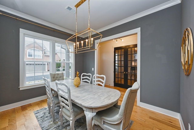 dining space with crown molding, light hardwood / wood-style flooring, french doors, and a chandelier