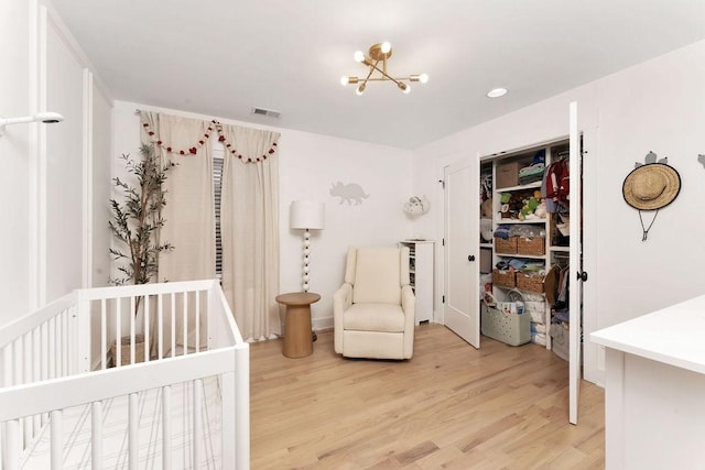 bedroom featuring hardwood / wood-style flooring, a nursery area, a notable chandelier, and a closet