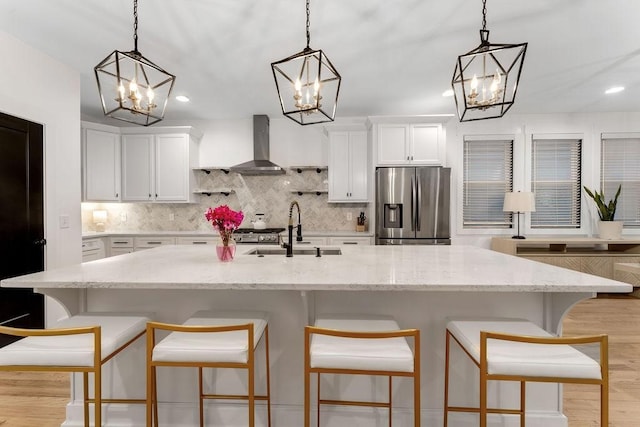 kitchen with stainless steel refrigerator with ice dispenser, sink, hanging light fixtures, white cabinets, and wall chimney range hood