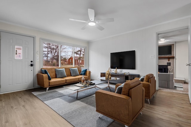 living room with crown molding, ceiling fan, a fireplace, and light hardwood / wood-style floors