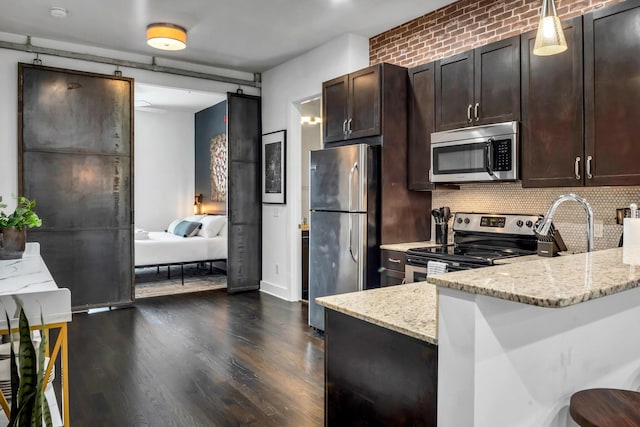 kitchen featuring light stone counters, pendant lighting, stainless steel appliances, and a kitchen breakfast bar