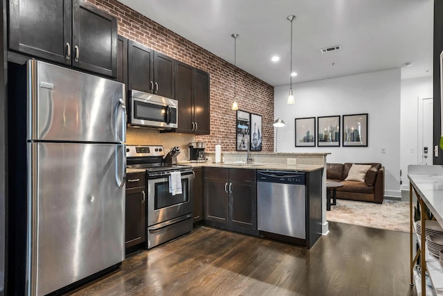 kitchen featuring pendant lighting, light stone counters, brick wall, and appliances with stainless steel finishes