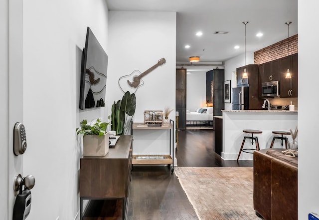 kitchen with dark wood-type flooring, decorative light fixtures, dark brown cabinets, appliances with stainless steel finishes, and kitchen peninsula