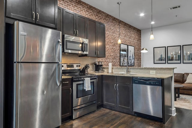 kitchen featuring sink, dark wood-type flooring, appliances with stainless steel finishes, hanging light fixtures, and light stone countertops