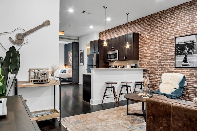 kitchen featuring stainless steel appliances, dark brown cabinets, a kitchen breakfast bar, dark hardwood / wood-style flooring, and brick wall