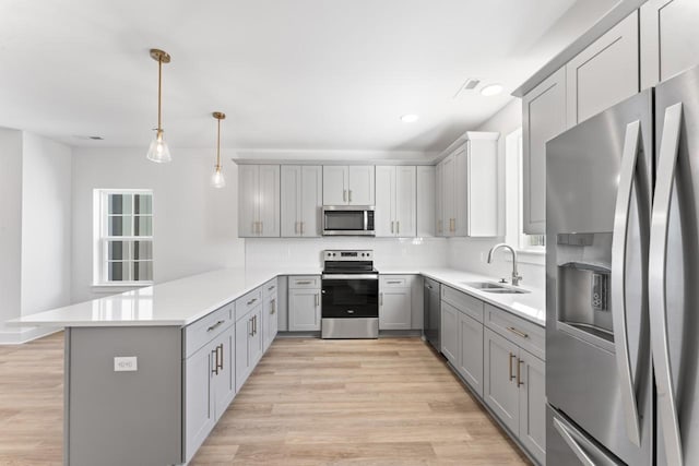 kitchen with gray cabinetry, stainless steel appliances, a peninsula, a sink, and light wood-type flooring