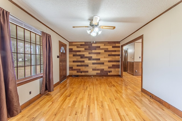 unfurnished room featuring crown molding, light hardwood / wood-style flooring, ceiling fan, wooden walls, and a textured ceiling