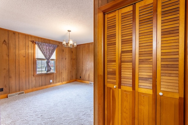 unfurnished room with an inviting chandelier, wood walls, a textured ceiling, and carpet flooring