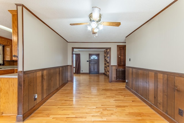 hall with crown molding, light hardwood / wood-style floors, a textured ceiling, and wood walls