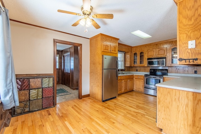 kitchen featuring sink, ornamental molding, ceiling fan, stainless steel appliances, and light wood-type flooring